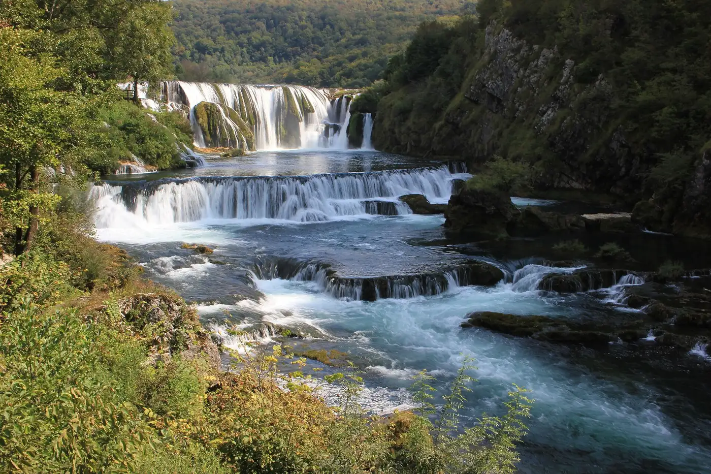Štrbački buk stepping down the emerald Una river between forested limestone banks near Donji Lapac